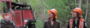 Two people looking up at trees with a skidder in the background